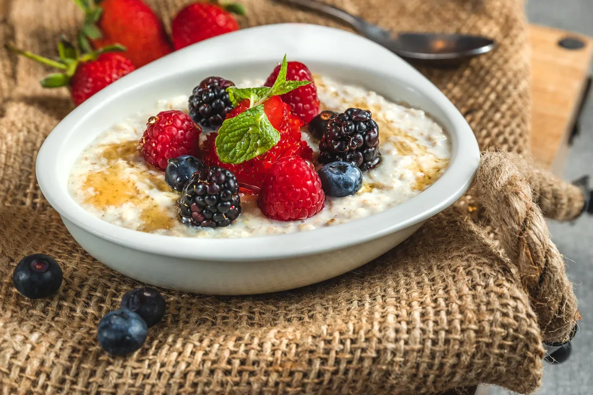 White bowl of creamy oats with mixed berries on a woven cloth.