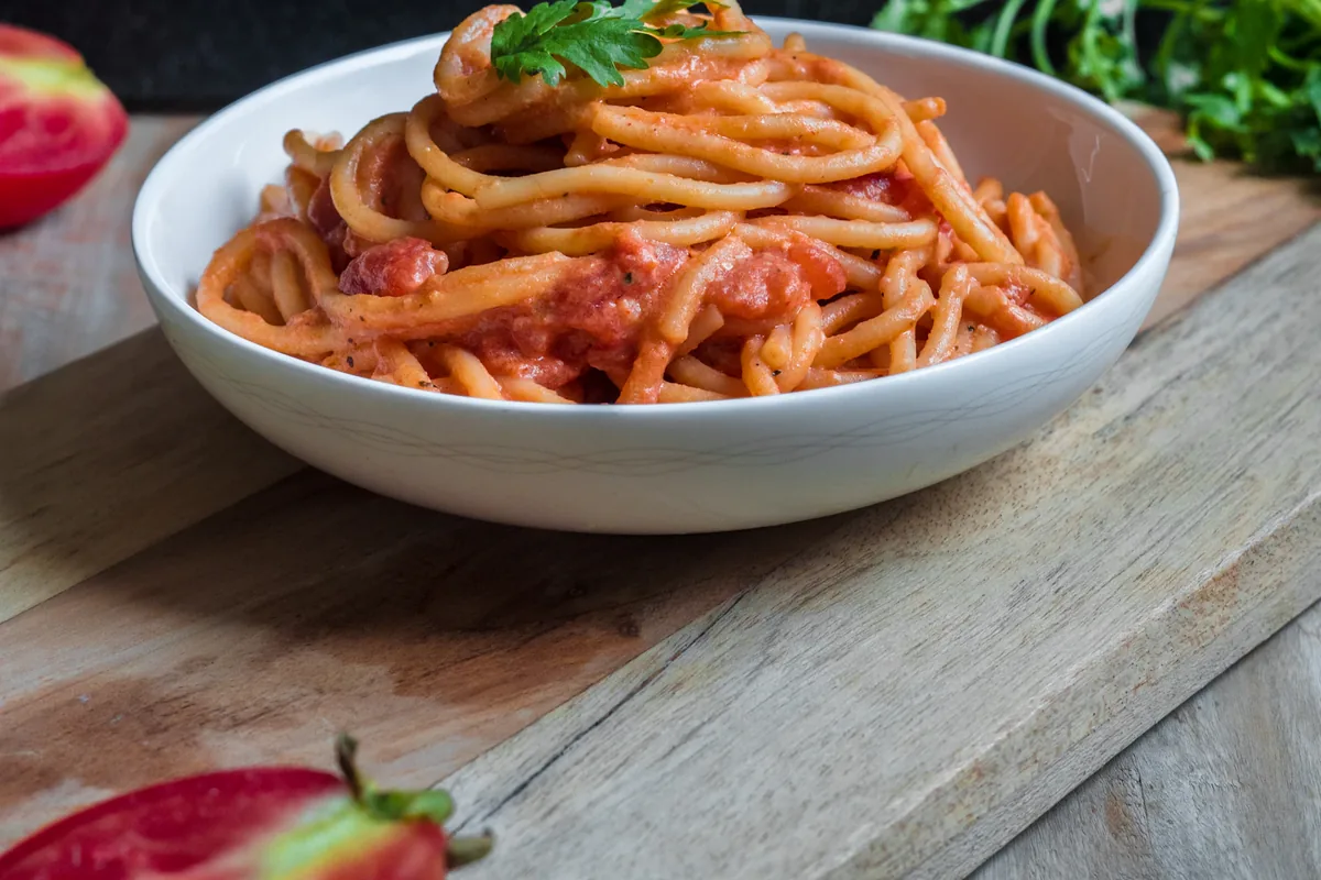 Spaghetti in red sauce with a green herb garnish in a white bowl.