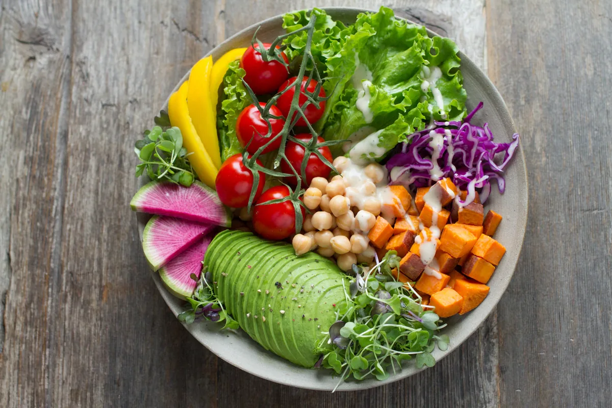 Colorful vegetable salad bowl with greens, avocado, tomatoes, chickpeas and sweet potato.